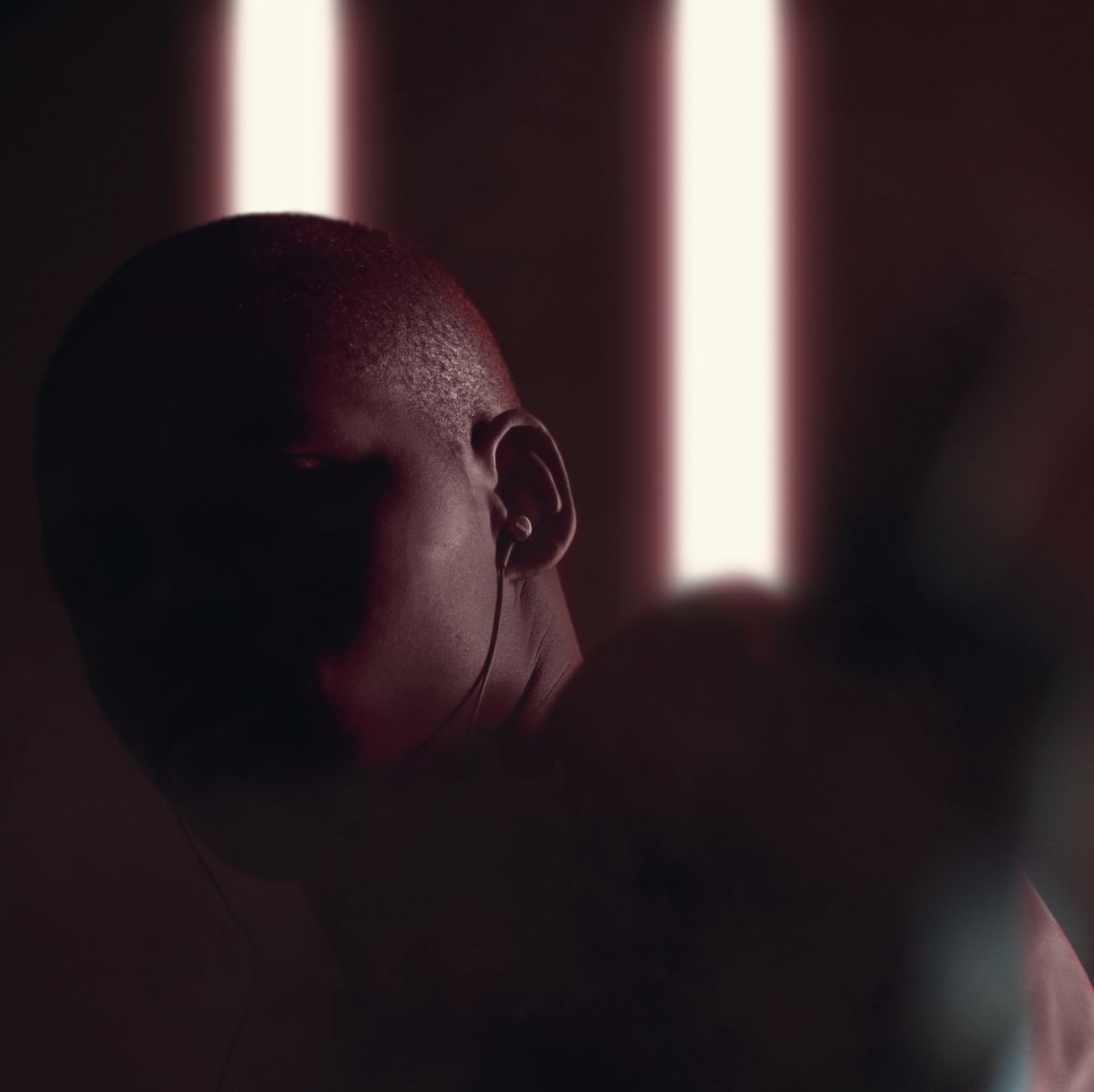 Dark and moody portrait of a person in earphones, highlighted by vertical backlights.